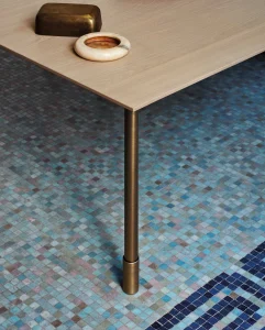 Tavolo elegante cucina cesar MAXIMA 2.2 STYLISH FLARE in legno chiaro con gambe metalliche brunite, posizionato su pavimento mosaico blu e turchese, creando un atmosfera moderna e raffinata per interni.