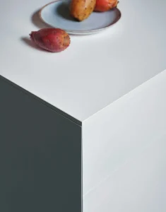 Tavolo moderno bianco con angoli netti, piatto trasparente e frutta rossa, design minimalista e materiali eleganti.