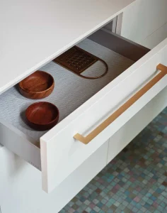 Cassetto bianco aperto con ciotole in legno e un vassoio, materiali moderni e stile minimalista. Design elegante e funzionale.