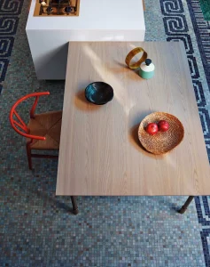 Tavolo in legno chiaro con ciotole nere e frutta, sedie moderne, pavimento mosaico. Design elegante e contemporaneo.